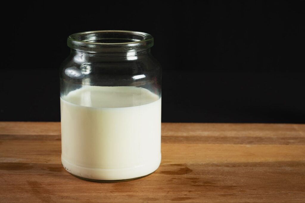 A glass jar filled with milk on a wooden surface against a black background, perfect for dairy-related themes.