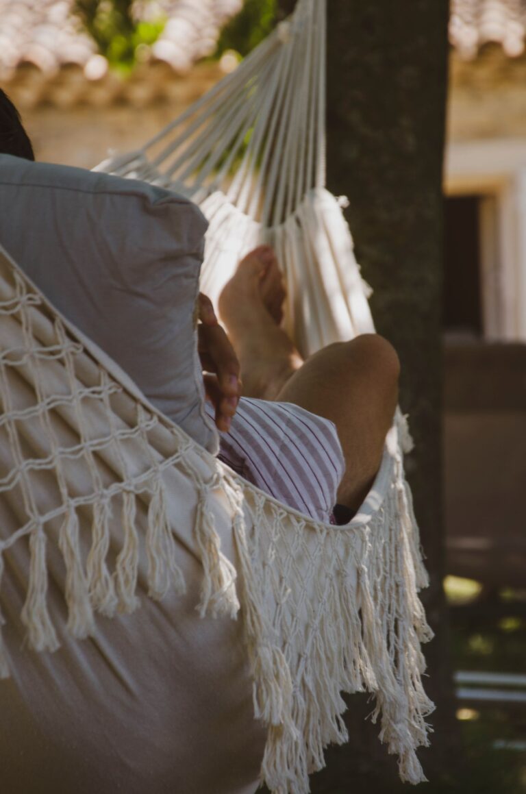 A person enjoys a restful moment in a hammock in a sun-dappled garden setting.