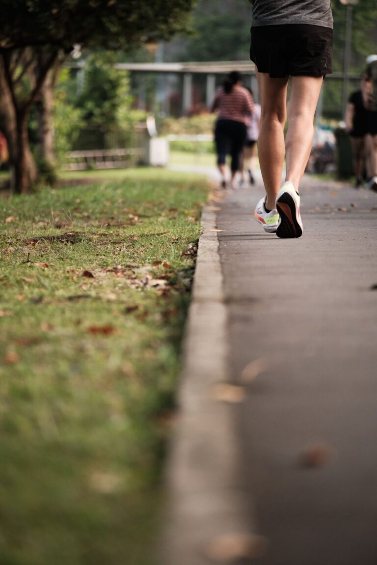 A person jogging on a park path surrounded by greenery and fellow walkers.