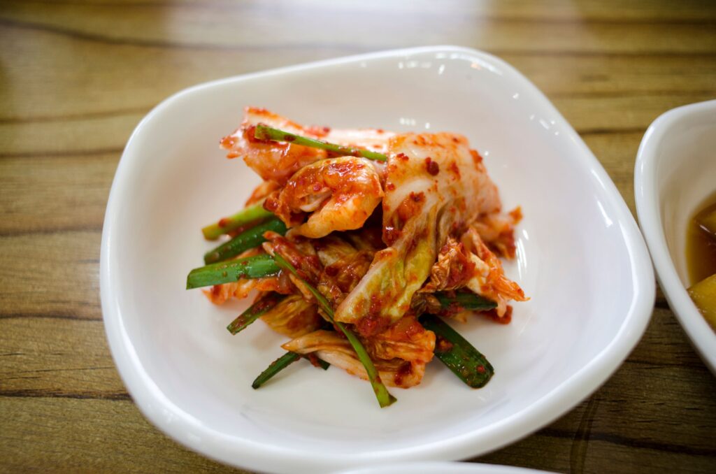Close-up of traditional Korean kimchi served in a white ceramic dish on a wooden table.