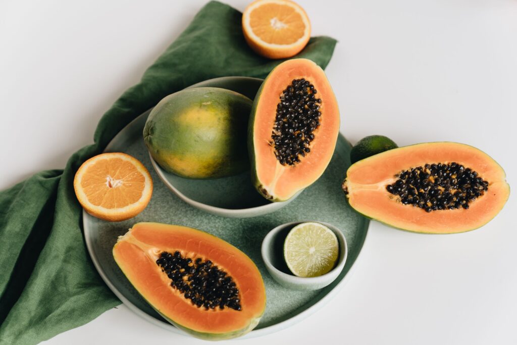 Colorful assortment of sliced tropical fruits, papaya and citrus, on a ceramic plate.