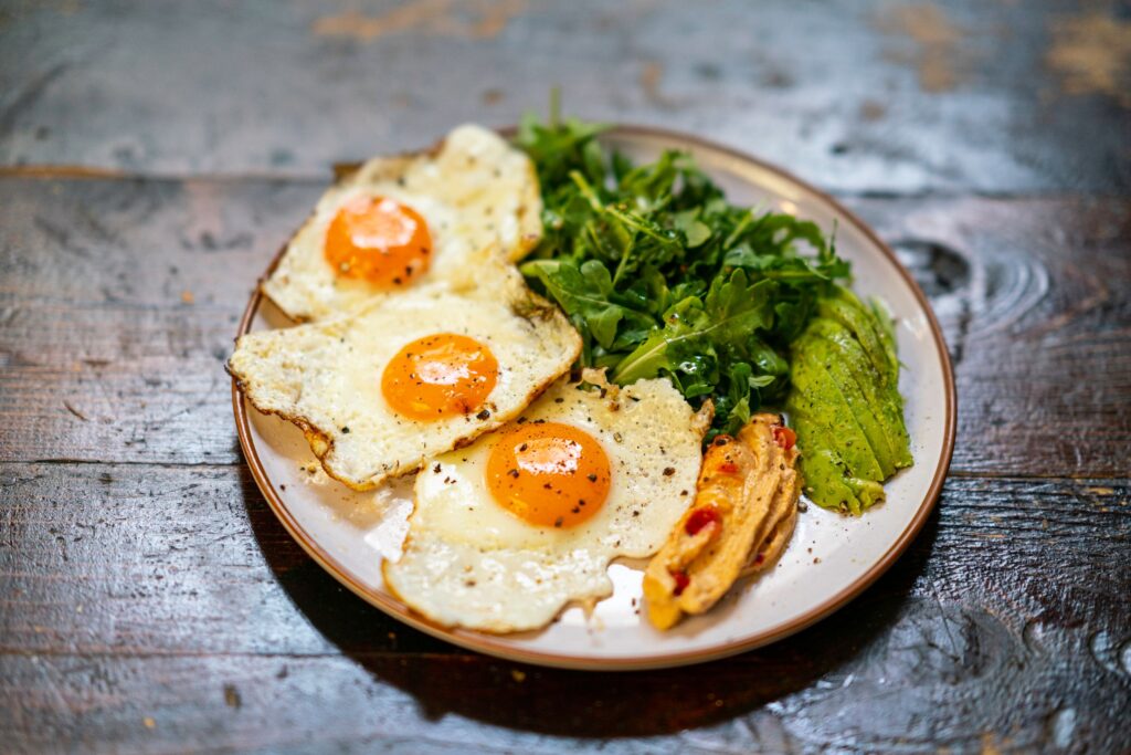 Delicious breakfast plate of fried eggs, arugula salad, and veggies.