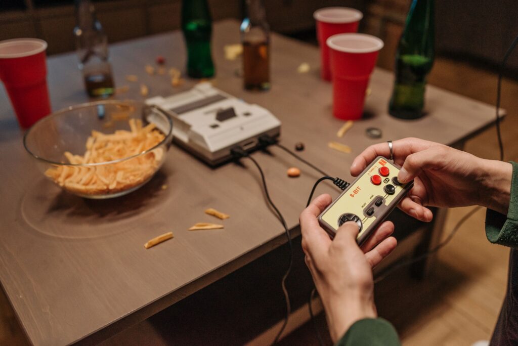 Hands holding a vintage game controller during a casual retro gaming night with snacks and drinks.
