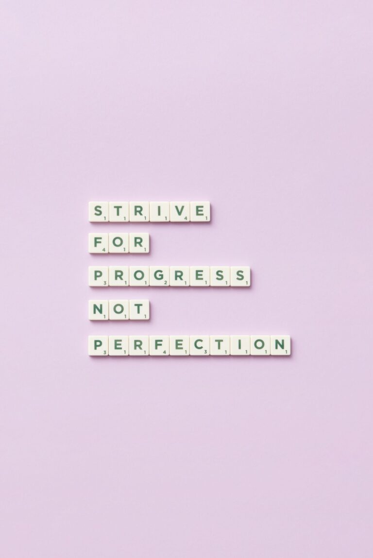 Scrabble tiles spelling 'Strive for progress, not perfection' on a pastel background.