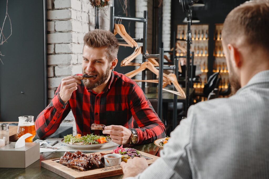 Two men enjoy a casual meal in a Kyiv restaurant featuring barbecue ribs and beer.