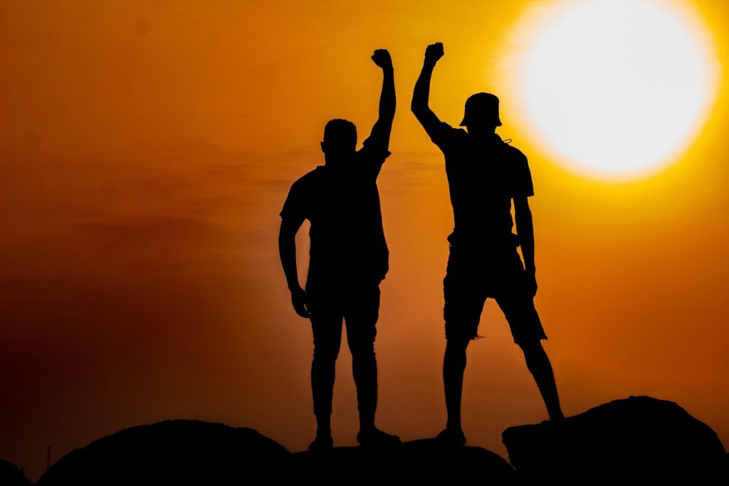 Two silhouetted figures raising fists triumphantly against a vibrant sunset in Ghana.