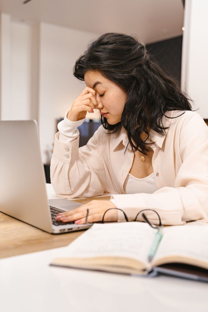 Woman with closed eyes feeling frustration while working on a laptop indoors.