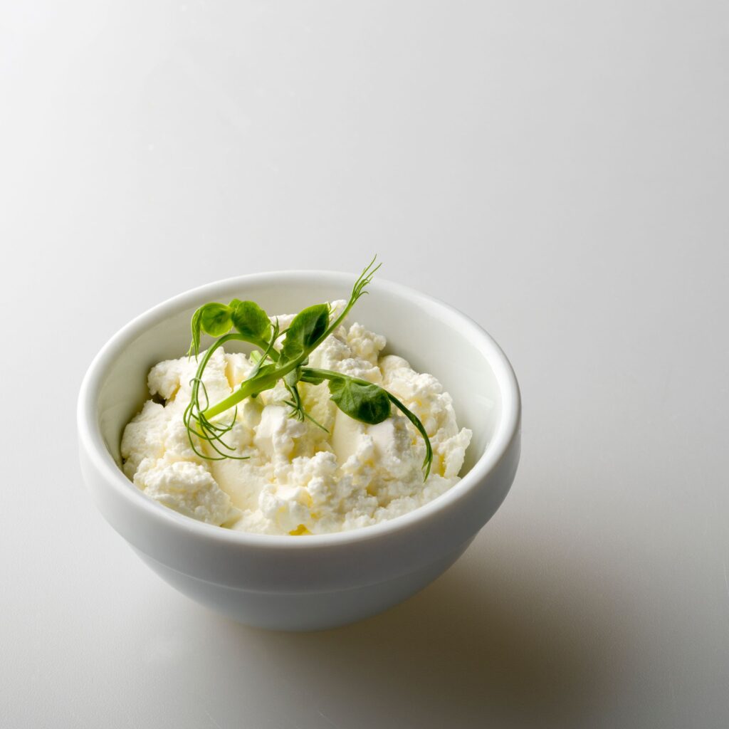 A clean and minimalistic shot of fresh cottage cheese garnished with pea shoots in a white bowl.