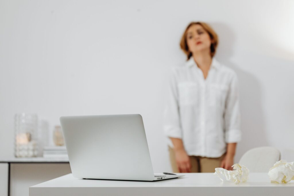 A laptop on a desk with a blurred background of a person standing, in a minimalist setting.