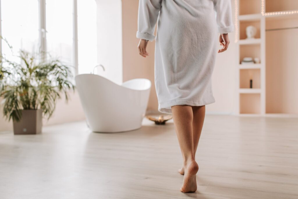 A person in a bathrobe walks towards a stylish bathtub in a bright, modern bathroom.
