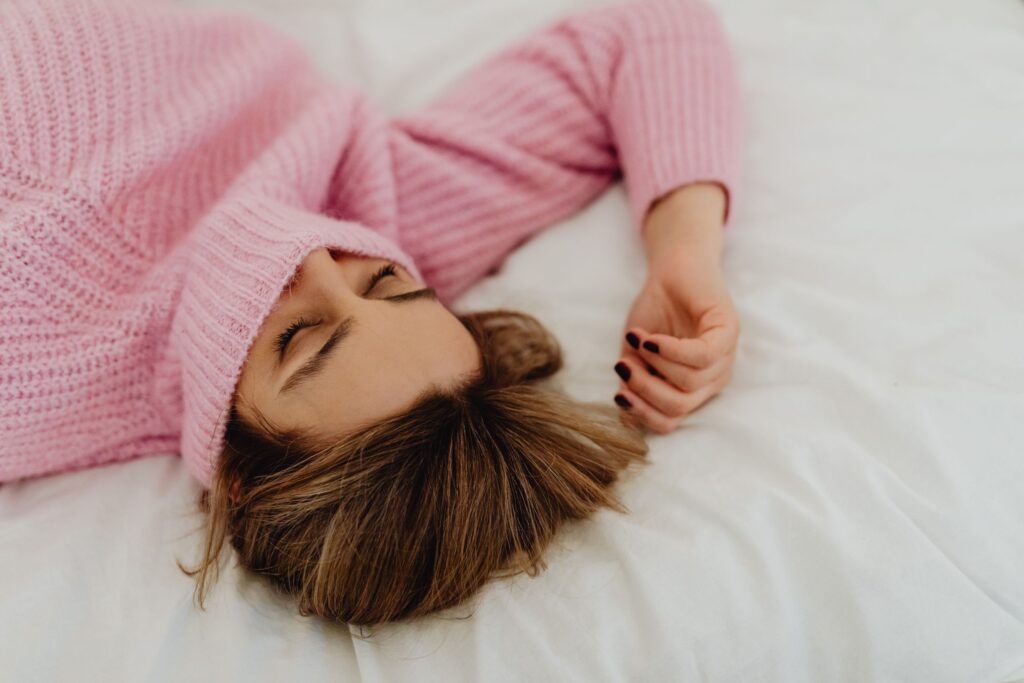A serene image of a woman in a pink sweater sleeping on a white bed.