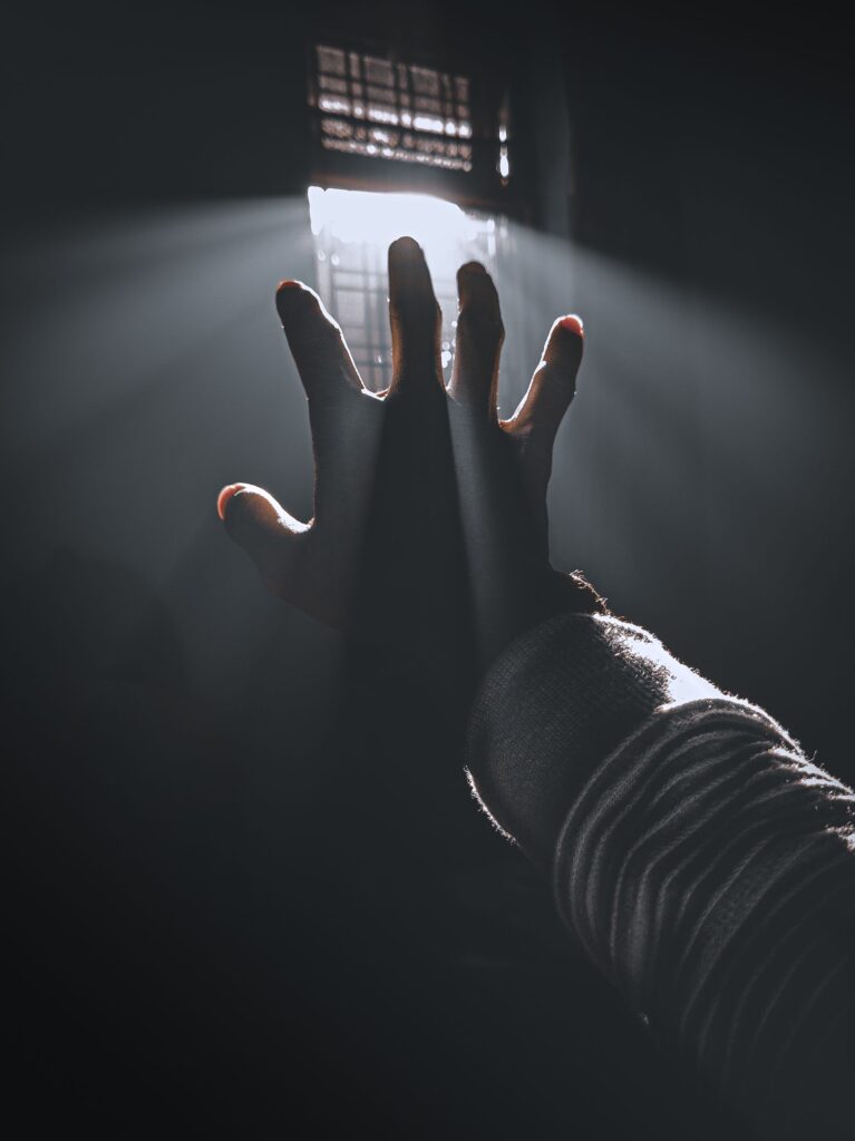A silhouetted hand reaching towards light rays beaming in through a window, evoking hope and inspiration.