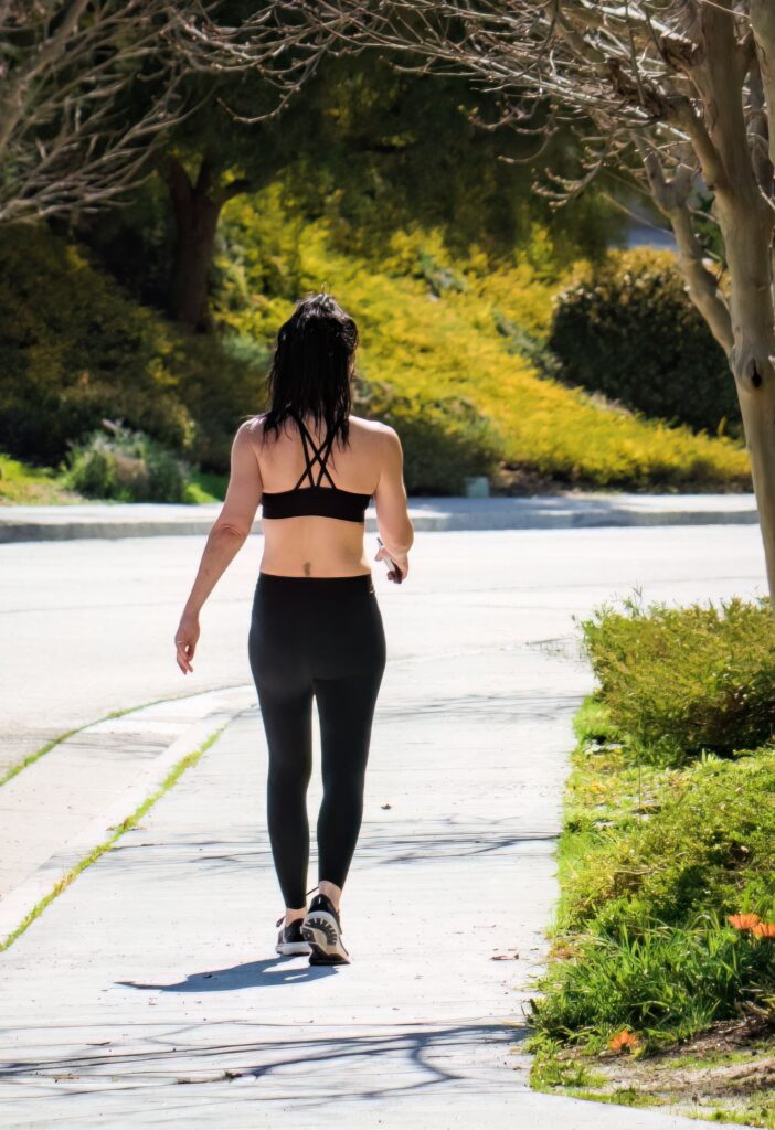 A woman exercises while strolling on a city sidewalk in activewear on a bright, sunny day.