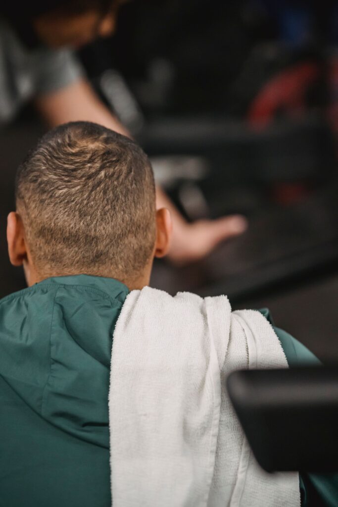 Back view of unrecognizable male with towel on shoulder sitting and resting after training in gym