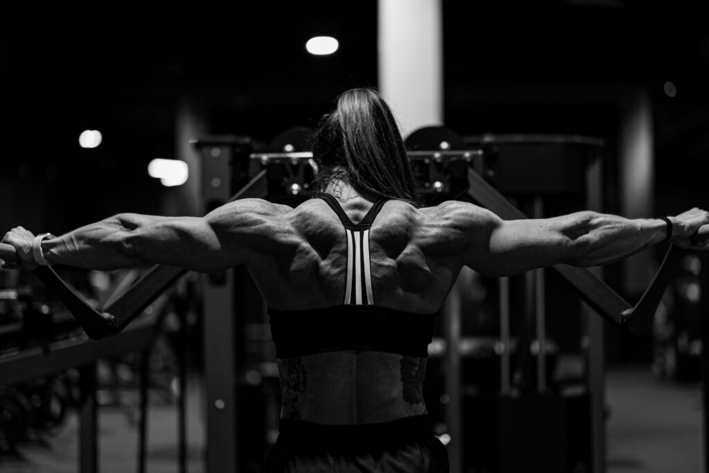 Black and white photo of a strong woman exercising in a gym with focus on back muscles.