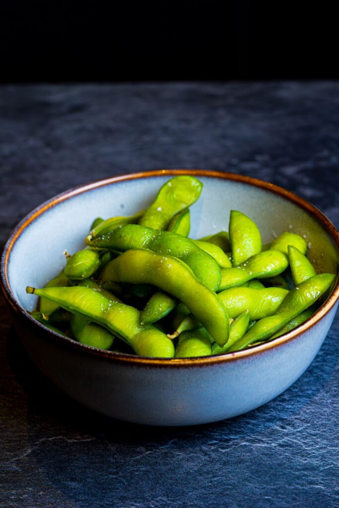 Bowl of fresh green edamame beans on a dark surface.
