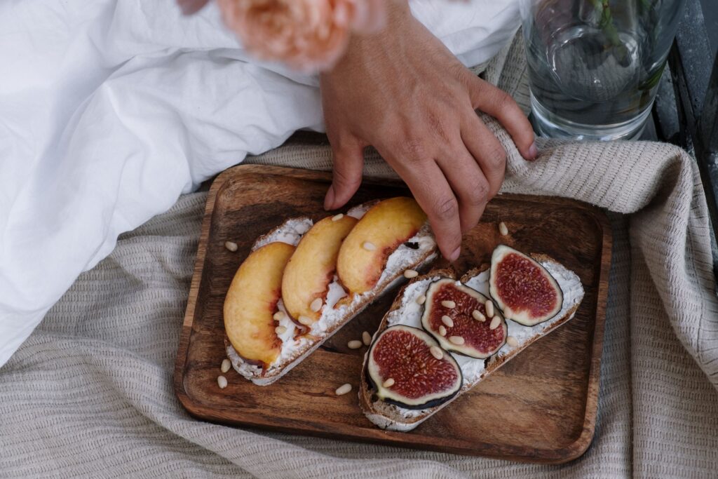 Close-up of artisan toast with fig and peach slices on a wooden tray, styled indoors.