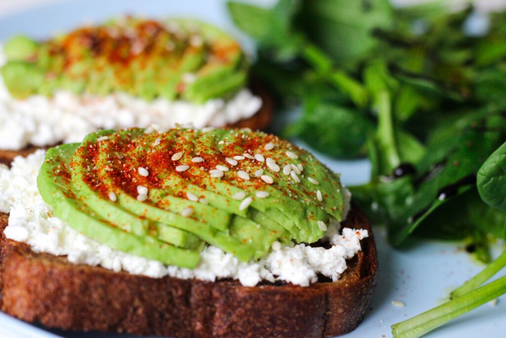 Close-up of avocado and cottage cheese on toast with leafy greens on a plate.