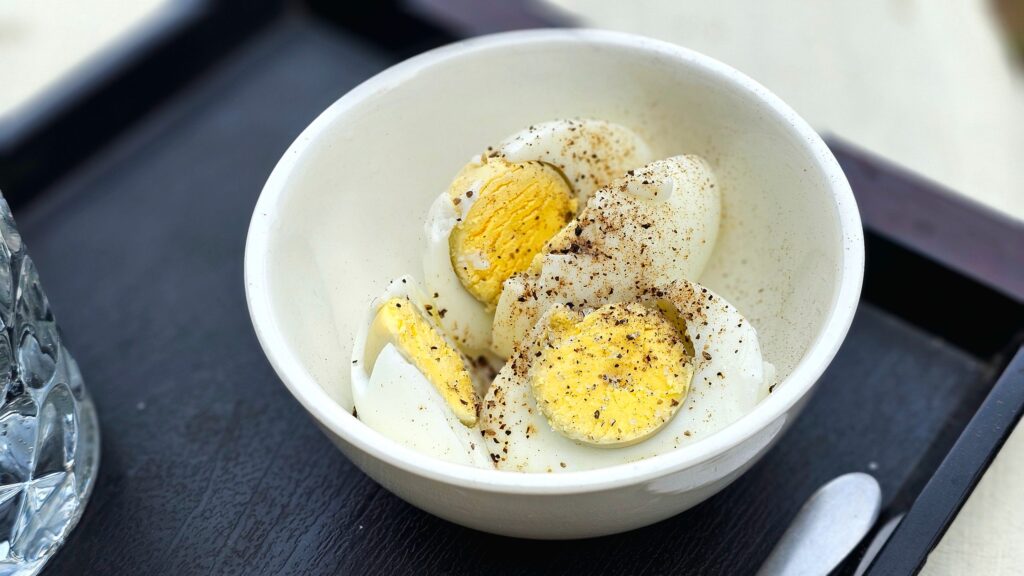 Close-up of sliced boiled eggs seasoned with pepper in a white bowl, ideal for breakfast or snack imagery.