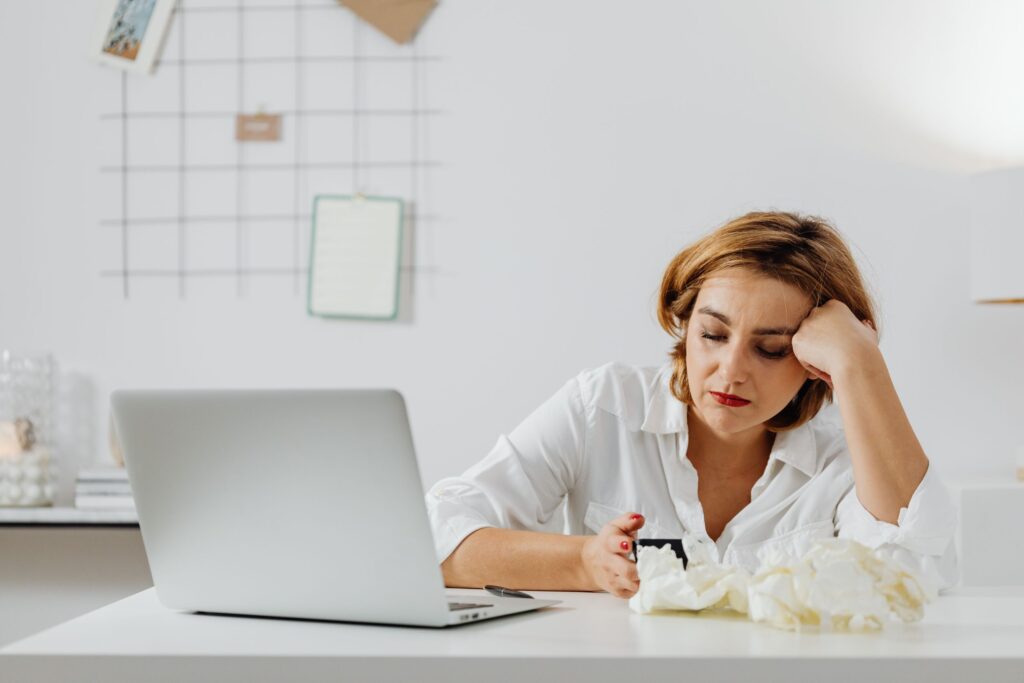 Exhausted woman working from home, surrounded by tissues, illustrating remote work challenges while feeling unwell.