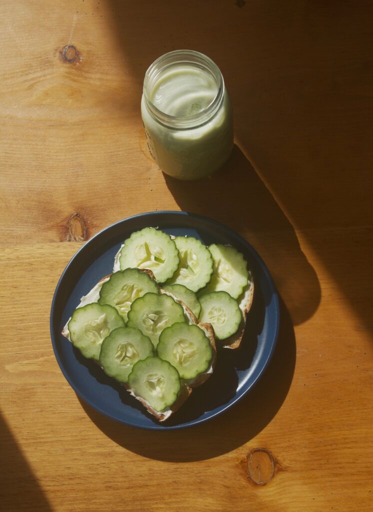 Flatlay of iced matcha latte and cucumber toast with artistic lighting on wooden table
