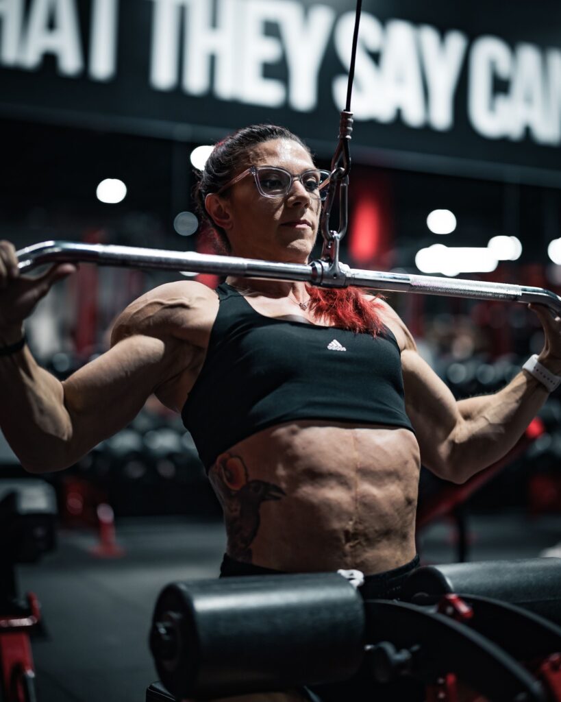 Focused woman lifting weights in a gym, showcasing strength and muscle definition.