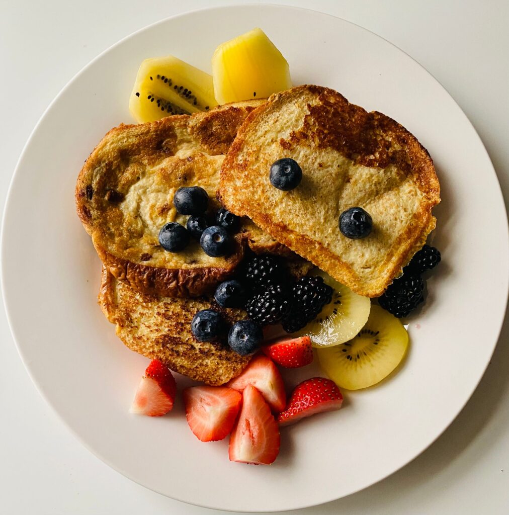 French toast served with fresh strawberries, blueberries, blackberries, and kiwi slices on a white plate.