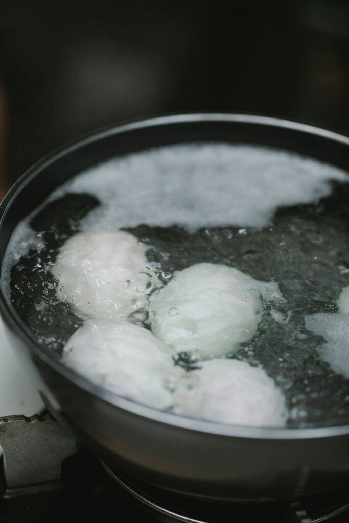 From above of metal pan filled with boiling water and eggs placed on stove