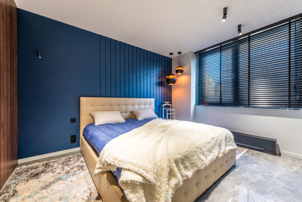 Plaid with pillows on bed against lamps and window blinds above tiled floor in contemporary bedroom