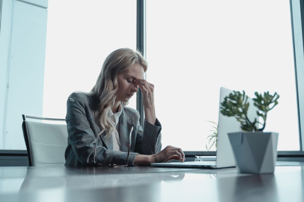 Professional woman in office, sitting at desk, looking stressed with laptop.