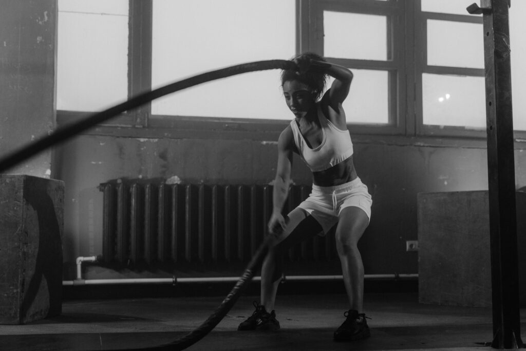 Woman in a gym engaging in vigorous battle rope workout for fitness.