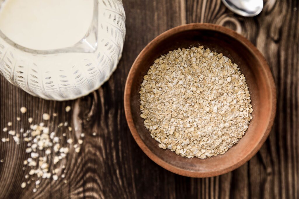 Wooden bowl of oats with milk jug on rustic table. Ideal for health-focused breakfast imagery.