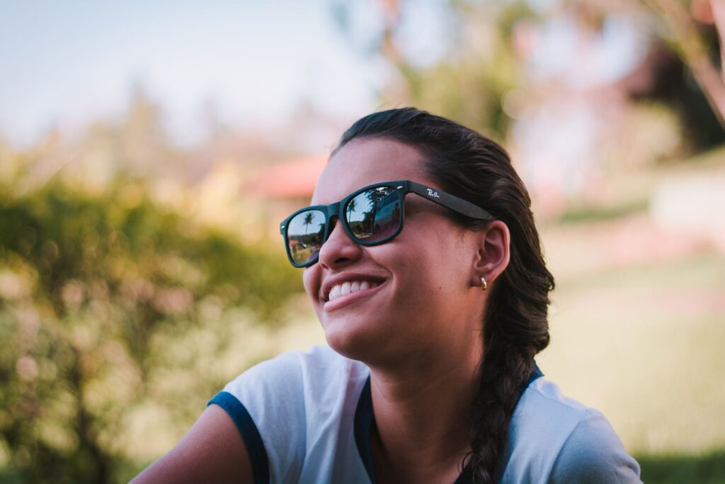 Young woman smiling outdoors wearing sunglasses, embracing a carefree summer vibe.